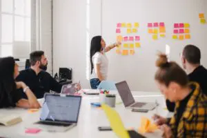 girl standing at white board with team brainstorming on employee experience