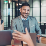 Corporate visibility; man and woman smiliing, sitting next to each other listening to woman sitting across speaking to them