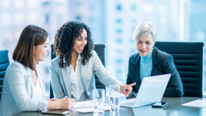 3 corporate, female talent sitting at a conference table, looking at a lap top