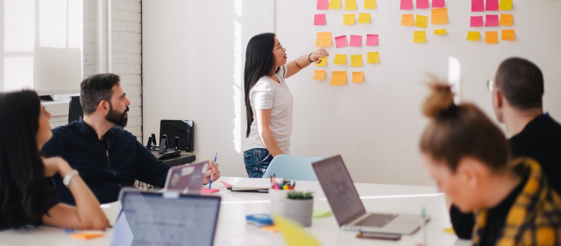 girl standing at white board with team brainstorming on employee experience