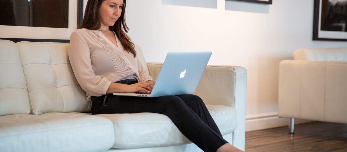 Woman sitting on a white couch with laptop on her lap