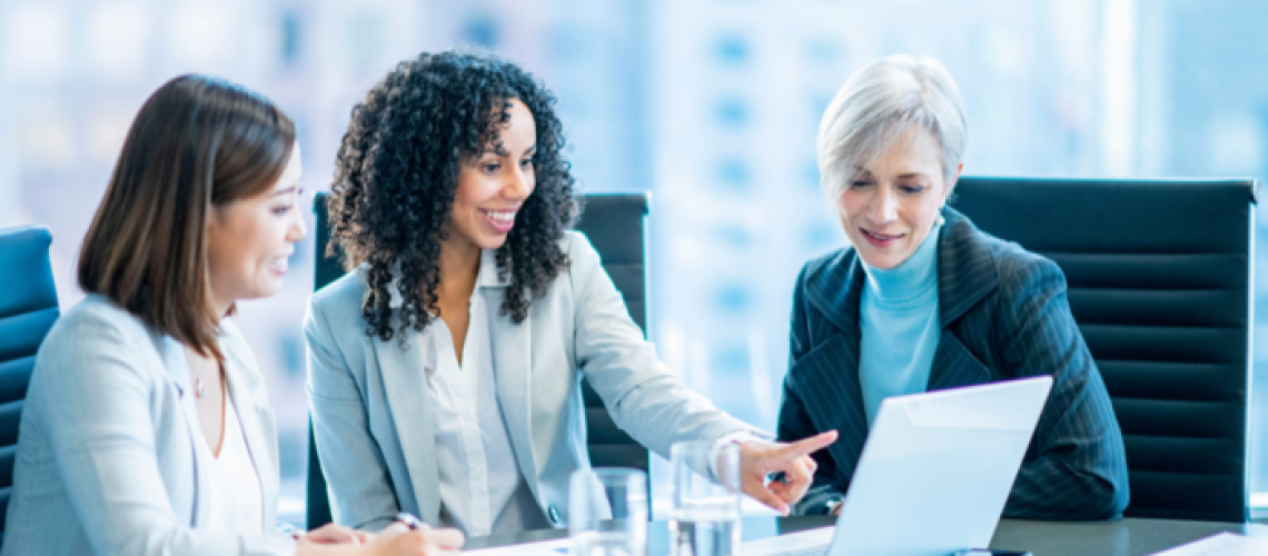 3 corporate, female talent sitting at a conference table, looking at a lap top