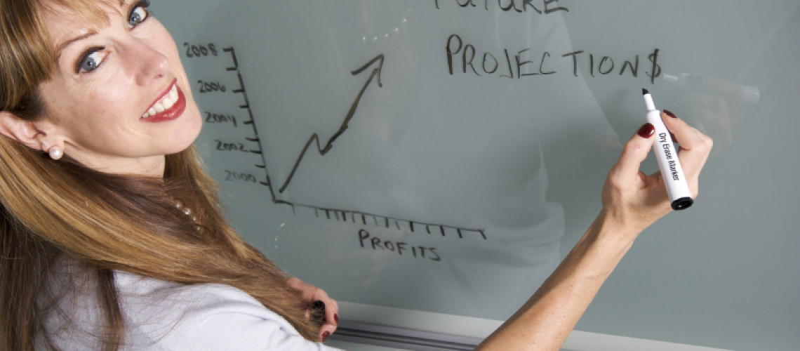 woman with white shirt writing future projections on white board looking at camera